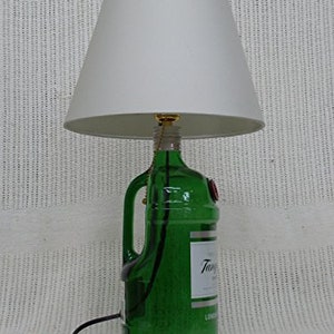 May include: A green glass bottle lamp with a white lampshade. The bottle has a label that says "Tanqueray" and "London Dry Gin".