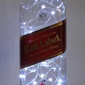 May include: A clear glass bottle with a red label that says "Johnnie Walker Red Label Blended Scotch Whisky Established 1820" with white string lights wrapped around it.