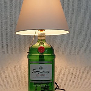 May include: A green glass bottle lamp with a white lampshade. The bottle is labeled "Tanqueray Imported London Dry Gin".
