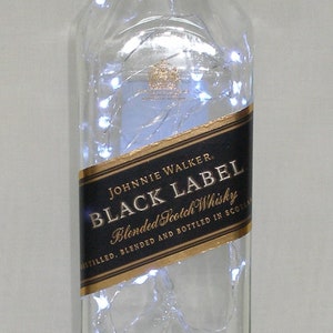 Peut inclure: Une bouteille en verre transparente avec une &eacute;tiquette noire qui indique "JOHNNIE WALKER. BLACK LABEL Blended Scotch Whisky DISTILLED, BLENDED AND BOTTLED IN SCOTLAND". La bouteille est d&eacute;cor&eacute;e de lumi&egrave;res blanches et d'une &eacute;tiquette dor&eacute;e qui indique "AGED 12 YEARS".