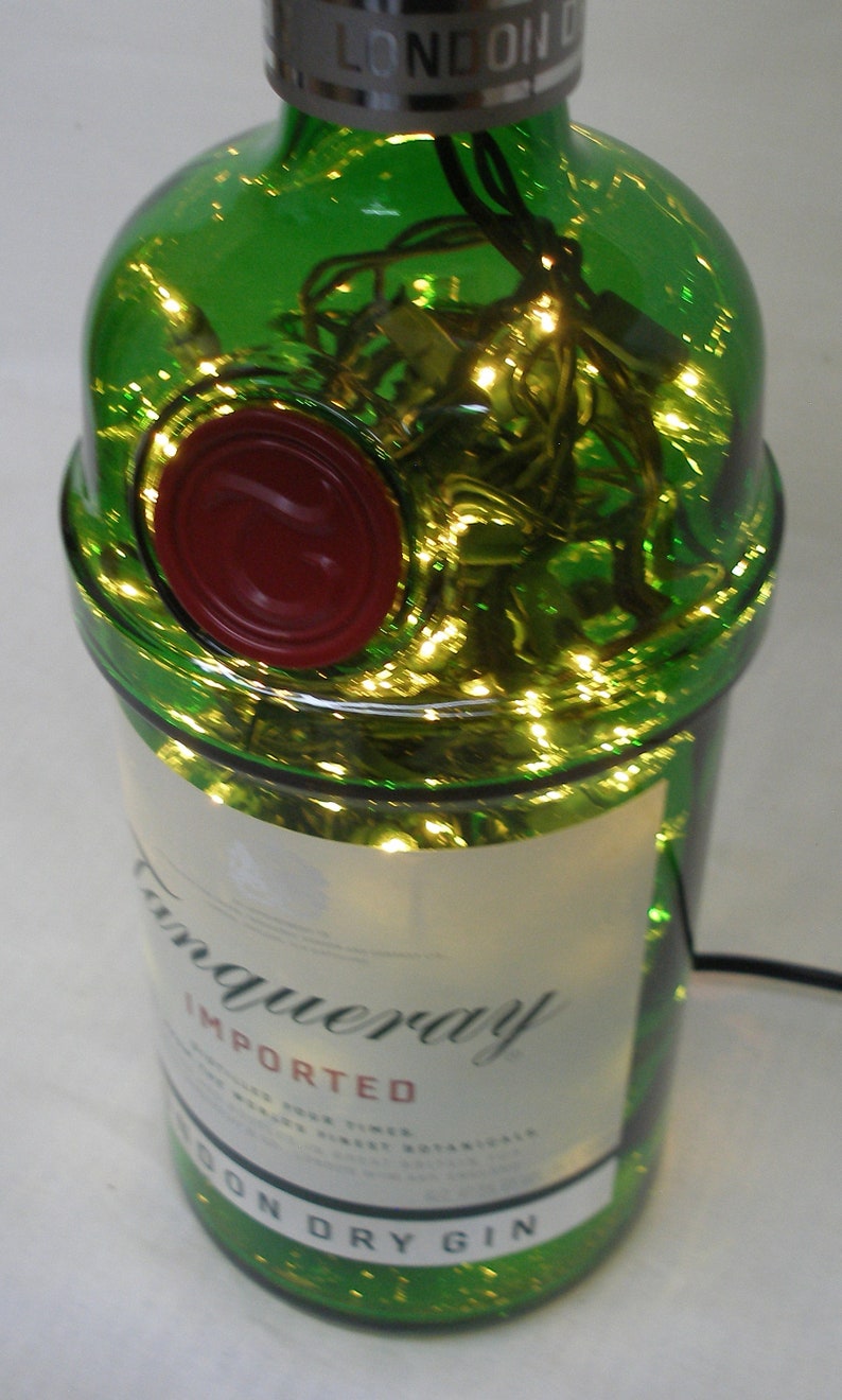 May include: A green glass bottle with a red wax seal and a white label that reads "Tanqueray Imported London Dry Gin". The bottle is filled with string lights.