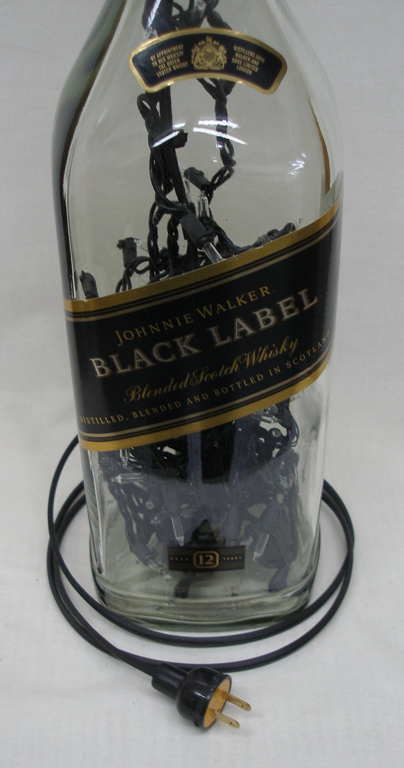 May include: A clear glass bottle with a black label that reads "JOHNNIE WALKER BLACK LABEL Blended Scotch Whisky DISTILLED, BLENDED AND BOTTLED IN SCOTLAND". The bottle is filled with black string lights and has a gold label with the text "12" on it.