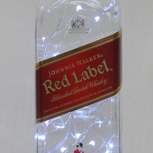 May include: A clear glass bottle with a red label that says "JOHNNIE WALKER. Red Label. Blended Scotch Whisky" and a gold label that says "ESTABLISHED 1820". The bottle is filled with white string lights.