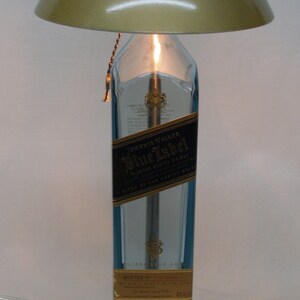 Pu&ograve; includere: Un'originale lampada da tavolo realizzata con una bottiglia di whisky Johnnie Walker Blue Label riciclata. La lampada presenta un paralume dorato metallico, una base argentata e una calda luce.