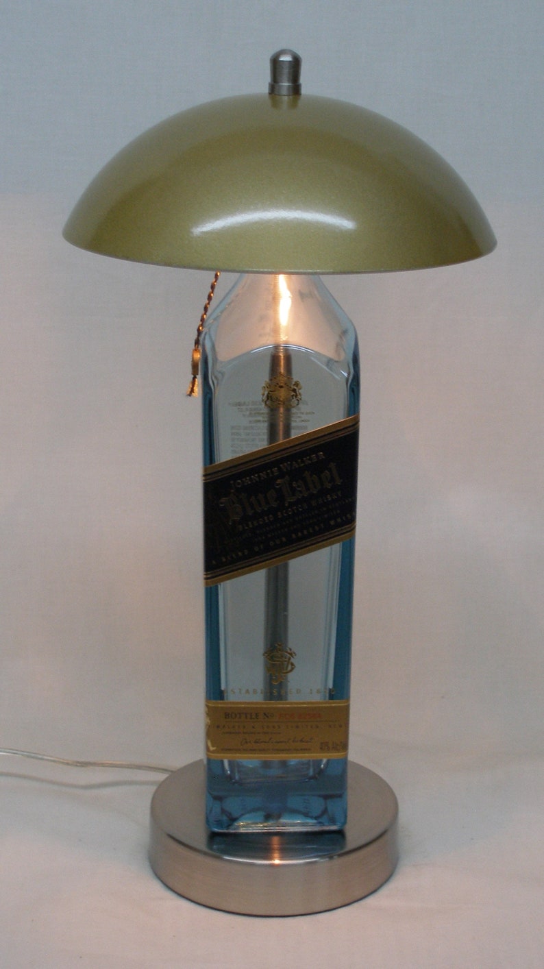 Pu&ograve; includere: Un'originale lampada da tavolo realizzata con una bottiglia di whisky Johnnie Walker Blue Label riciclata. La lampada presenta un paralume dorato metallico, una base argentata e una calda luce.