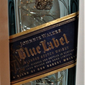 K&ouml;nnte beinhalten: Eine durchsichtige Glasflasche mit Johnnie Walker Blue Label Blended Scotch Whisky. Das Etikett ist gold und blau mit dem Text "Johnnie Walker Blue Label" und "Eine Mischung aus unseren seltensten Whiskys". Die Flasche hat einen Alkoholgehalt von 40%.