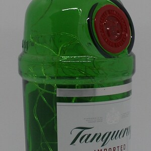 Puede incluir: Una botella de vidrio verde de Tanqueray London Dry Gin. La botella tiene una tapa plateada con el texto "LONDON DRY GIN" impreso en ella. La etiqueta es blanca con el texto "Tanqueray" en escritura verde y "IMPORTED" en negro. La botella es de 375 ml.