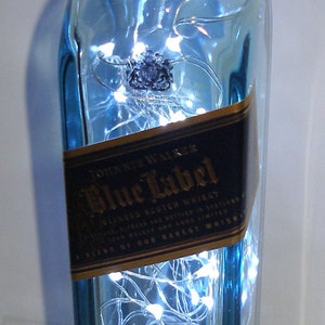 May include: A blue glass bottle with a gold label that reads "Johnnie Walker Blue Label Blended Scotch Whisky". The bottle is filled with white string lights.