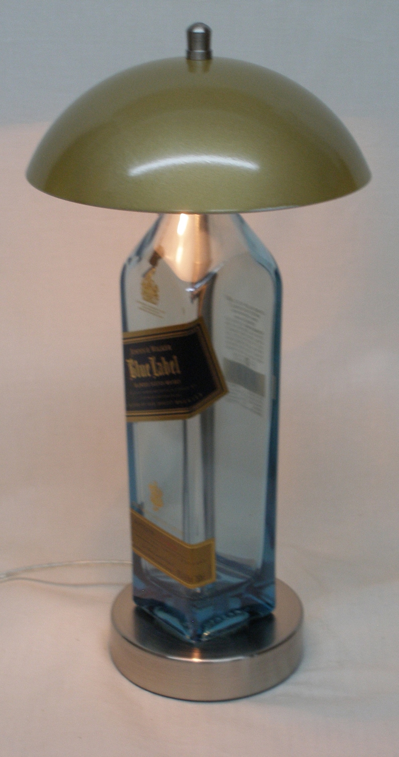 Pu&ograve; includere: Una lampada da tavolo unica realizzata con una bottiglia riciclata di Johnnie Walker Blue Label. Presenta un paralume dorato metallico e una base argentata. L'etichetta originale della bottiglia &egrave; visibile.