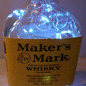 May include: A clear glass bottle with a brown label that reads "Maker's IV Mark Kentucky Straight Bourbon Whisky Handmade". The bottle is decorated with white string lights.