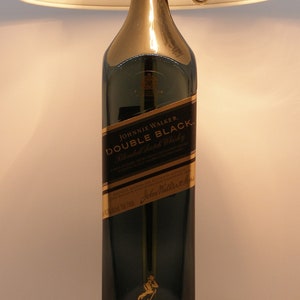 May include: A black lampshade with a gold base and a clear glass bottle with a gold label that reads "Johnnie Walker Double Black Blended Scotch Whisky".