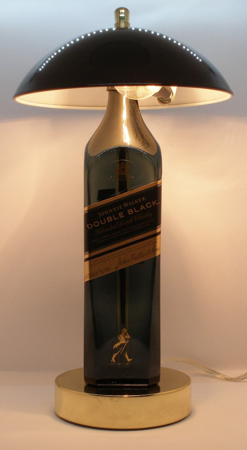 May include: A black lampshade with a gold base and a clear glass bottle with a gold label that reads "Johnnie Walker Double Black Blended Scotch Whisky".