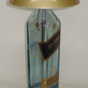 Pu&ograve; includere: Una lampada da tavolo unica realizzata con una bottiglia di whisky Johnnie Walker Blue Label riciclata. La lampada presenta un paralume color oro e una base in metallo spazzolato. La bottiglia conserva la sua etichetta originale ed &egrave; riempita con un liquido blu.