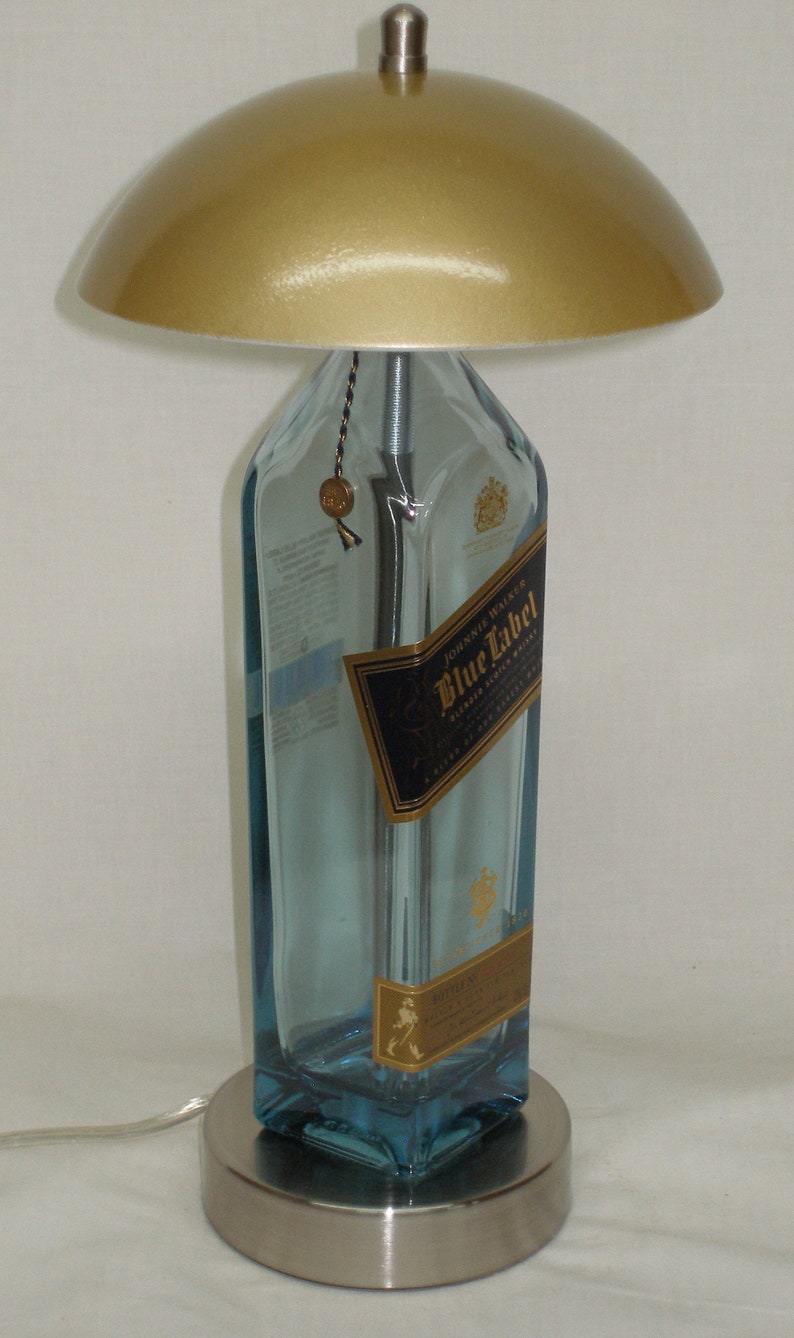 Pu&ograve; includere: Una lampada da tavolo unica realizzata con una bottiglia di whisky Johnnie Walker Blue Label riciclata. La lampada presenta un paralume color oro e una base in metallo spazzolato. La bottiglia conserva la sua etichetta originale ed &egrave; riempita con un liquido blu.