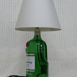 May include: A green glass bottle lamp with a white lampshade. The bottle is labeled "Tanqueray" and "London Dry Gin".