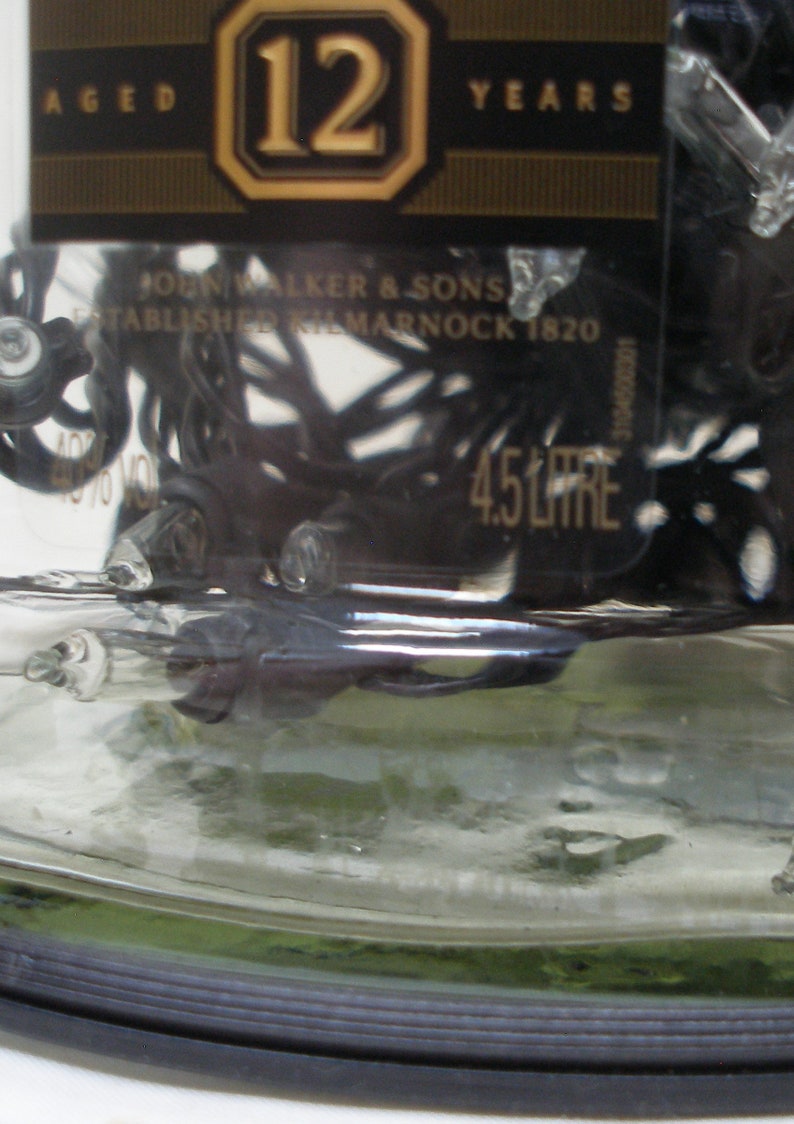 May include: A clear glass bottle with a black label that reads "AGED 12 YEARS" and "JOHN WALKER & SONS ESTABLISHED KILMARNOCK 1820". The bottle is filled with a dark liquid and has a black plastic cap.
