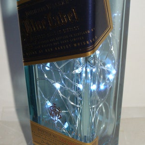 K&ouml;nnte beinhalten: Eine klare Glasflasche mit blauer T&ouml;nung, gef&uuml;llt mit wei&szlig;en LED-Lichtern. Die Flasche hat ein goldenes und blaues Etikett mit der Aufschrift "Johnnie Walker Blue Label" und "A Blend of Our Rarest Whiskies".