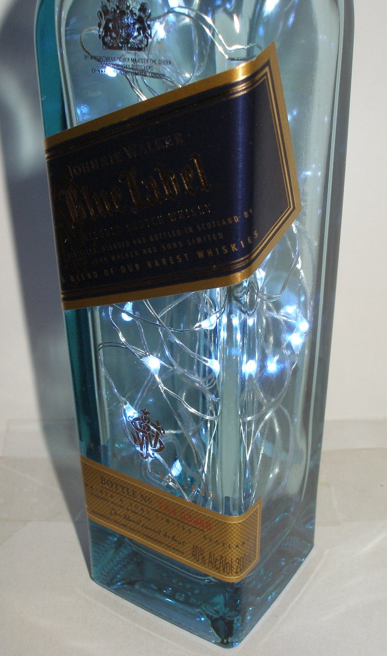 K&ouml;nnte beinhalten: Eine klare Glasflasche mit blauer T&ouml;nung, gef&uuml;llt mit wei&szlig;en LED-Lichtern. Die Flasche hat ein goldenes und blaues Etikett mit der Aufschrift "Johnnie Walker Blue Label" und "A Blend of Our Rarest Whiskies".