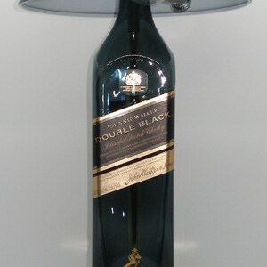 May include: A black lamp with a gold base and a black lampshade. The lamp is made from a repurposed Johnnie Walker Double Black Blended Scotch Whisky bottle.