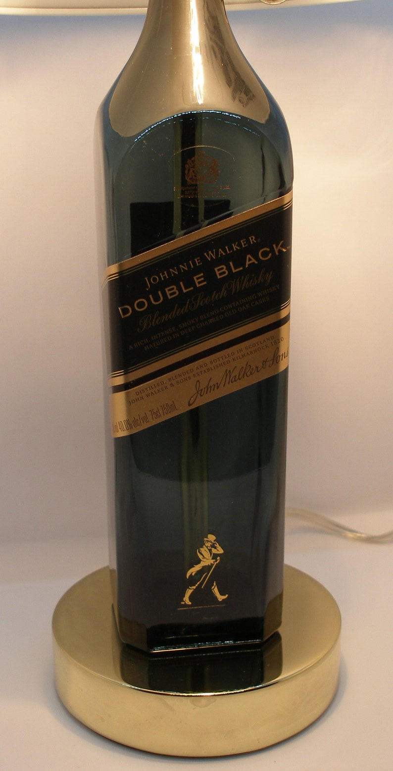 May include: A dark green glass bottle of Johnnie Walker Double Black Blended Scotch Whisky. The bottle has a gold label with the brand name and a description of the whisky. The bottle is sitting on a gold metal base.