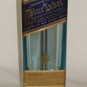 Pu&ograve; includere: Una bottiglia di vetro blu di whisky scozzese Johnnie Walker Blue Label. La bottiglia ha una forma rettangolare e una base metallica. L'etichetta &egrave; blu e oro, con il nome del marchio e altri dettagli.