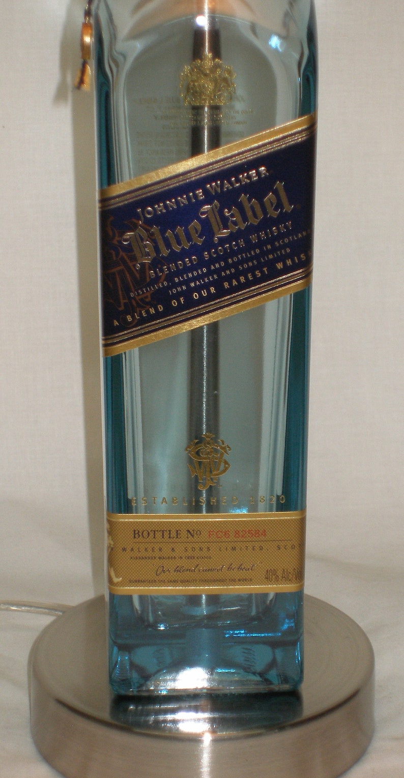 Pu&ograve; includere: Una bottiglia di vetro blu di whisky scozzese Johnnie Walker Blue Label. La bottiglia ha una forma rettangolare e una base metallica. L'etichetta &egrave; blu e oro, con il nome del marchio e altri dettagli.