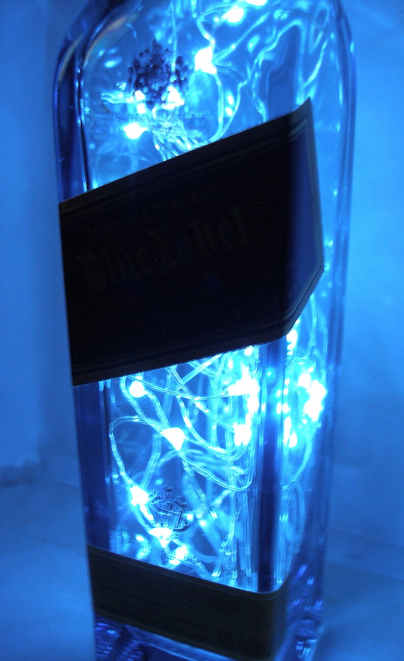 K&ouml;nnte beinhalten: Eine durchsichtige Glasflasche mit einem blauen Etikett, auf dem "Black Label" steht, ist mit blauen LED-Lichtern gef&uuml;llt.