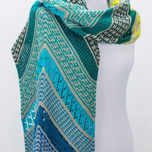 Könnte beinhalten: Ein dreieckiger Schal mit einem geometrischen Muster in Blautönen, Grün und Beige. Der Schal ist mit verschiedenen Maschen gestrickt, darunter Spitze und Kabel.