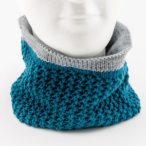 Könnte beinhalten: Ein türkisfarbener gestrickter Halsschmuck mit grauem Besatz. Der Halsschmuck ist aus einem weichen, bequemen Material gefertigt und perfekt, um sich im Winter warm zu halten.