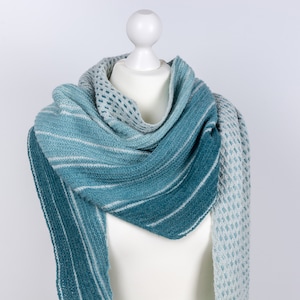 May include: A teal and white striped knitted scarf with a textured pattern. The scarf is draped over a white mannequin.