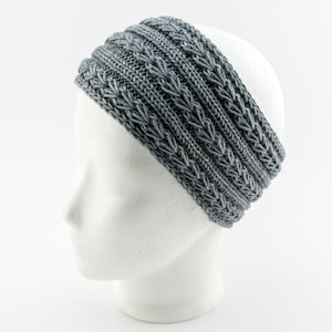 Könnte beinhalten: Grauer Strick-Stirnband mit Zopfmuster. Das Stirnband befindet sich auf einem weißen Mannequin-Kopf.