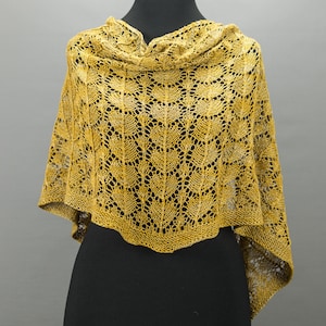 Puede incluir: Un chal de punto amarillo con un delicado patrón de encaje. El chal está drapeado sobre un maniquí negro.