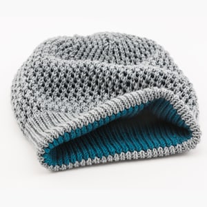 Puede incluir: Gorro de punto gris con forro de punto azul turquesa. El gorro tiene un tejido suelto y abierto.