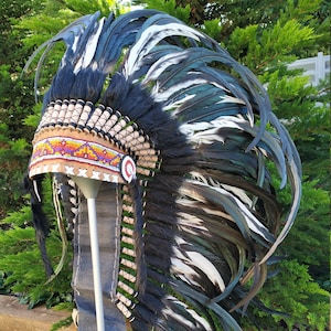 Peut inclure: Une coiffe de plumes noires et blanches avec une bande de perles. La coiffe est sur un support et a un design long et fluide.