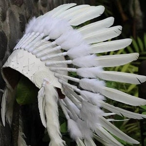 Peut inclure: Une coiffe de plumes blanches avec une base en cuir. Les plumes sont disposées en cercle et sont toutes blanches.