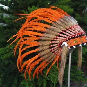 Könnte beinhalten: Orange-braunes Indianer-Kopfschmuck mit Federn und Perlen.