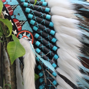 K&ouml;nnte beinhalten: Ein indianischer Kopfschmuck mit wei&szlig;en Federn, schwarzem und blauem Besatz und Perlenverzierungen.