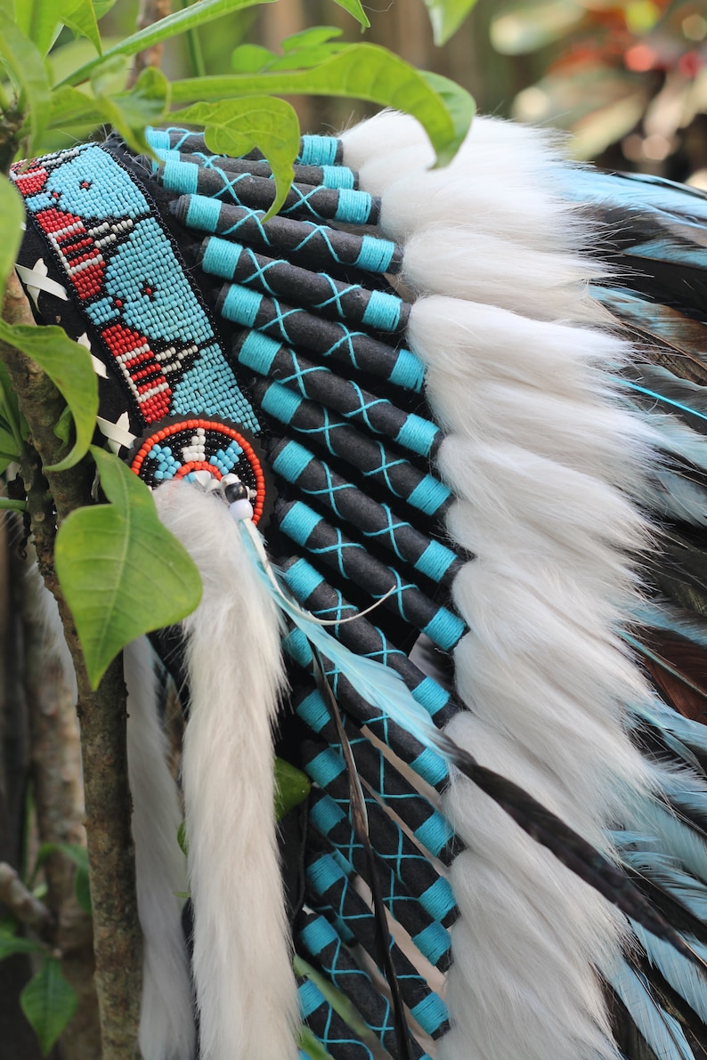 K&ouml;nnte beinhalten: Ein indianischer Kopfschmuck mit wei&szlig;en Federn, schwarzem und blauem Besatz und Perlenverzierungen.