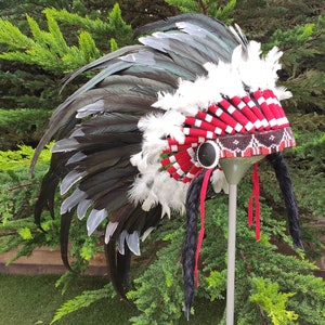 May include: A black and white feather headdress with red and white beaded trim. The headdress is on a stand and has black braids hanging down.