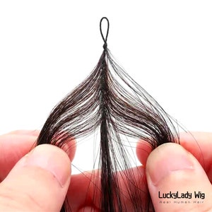 May include: Close-up of a weft of dark brown human hair extensions. The hair is held in place by a black elastic band.