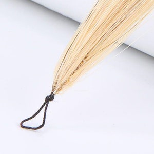 May include: A close-up of a light blonde hair extension with a black string tie at the end.