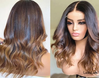 May include: A brown and blonde ombre human hair wig with loose waves. The wig is styled with a middle part and has a lace front.