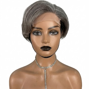 May include: A short, grey wig with a side parting, presented on a mannequin head. The wig features a realistic hairline and is complemented by a sparkling rhinestone necklace. The mannequin has dark lipstick and eye makeup.