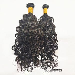 May include: Two bundles of dark brown, curly hair extensions. The hair is tightly curled and appears to be human hair. The top of each bundle is secured with a gold-coloured band. The text "LuckyLady Wig Real Human Hair" is visible at the bottom.