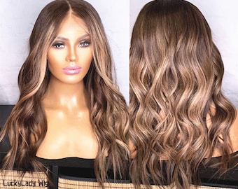 May include: A long, wavy, brown wig with blonde highlights. The wig is styled with loose waves and has a natural-looking parting. The wig is shown on a mannequin head.