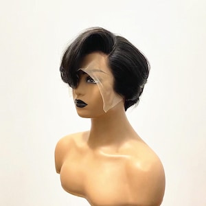 以下が含まれることがあります： サイドスイープのバングとシアーなレースフロントパネルを備えた、レイヤー入りの短い黒いピクシーカットウィッグ。髪は頭頂部にボリュームを持たせてスタイリングされており、ダークな唇と明確な顔立ちを持つ滑らかなマネキンの頭部に装着されています。