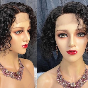 May include: A short, curly black wig with a lace front. The wig is styled with a side part and has a natural, voluminous look. The wig is worn by a mannequin with a pink jeweled necklace and earrings.