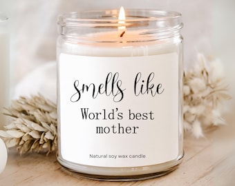 May include: A lit soy wax candle in a clear glass jar. The label reads "Smells like World's best mother." The candle is surrounded by dried flowers. The text "Natural soy wax candle" is at the bottom of the label.