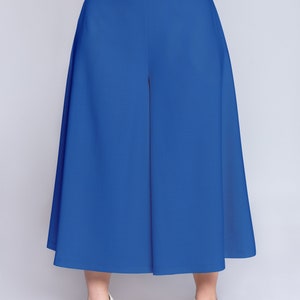 May include: Bright blue culottes with a high waist and wide legs. The trousers are a mid-calf length. The model is wearing white sandals. The culottes are a stylish, contemporary garment, suitable for various occasions.
