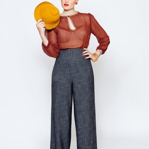May include: A woman wearing a red sheer blouse with a keyhole neckline, high-waisted wide-leg pants, and a yellow hat.